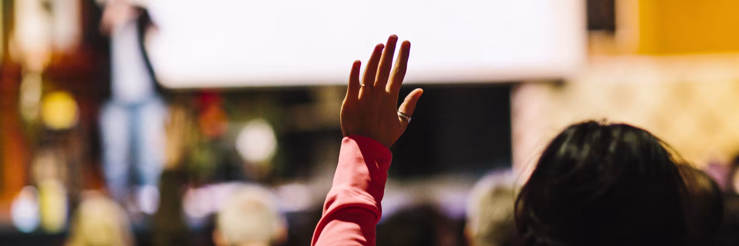 woman in the crowd raising her hand at a seminar